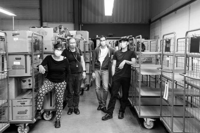 quatre personnes portant des masques respiratoires dans un atelier comportant des chariots à roulettes. Photo en noir et blanc