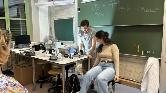 A seated woman and a standing man demonstrate at a workshop. They look at a computer together.