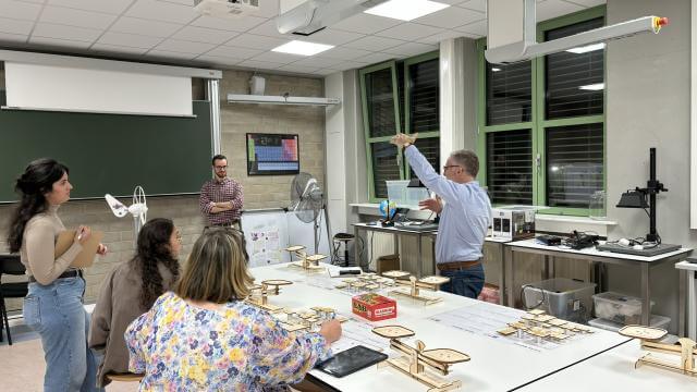 A group of adults take part in a workshop. Standing around a table, they discuss an exercise.