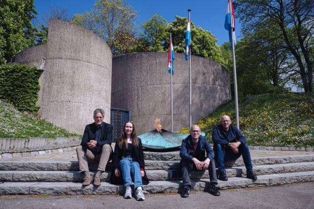trois hommes et une femme sont assis sur des escaliers devant le monument de la deuxième Guerre Mondiale