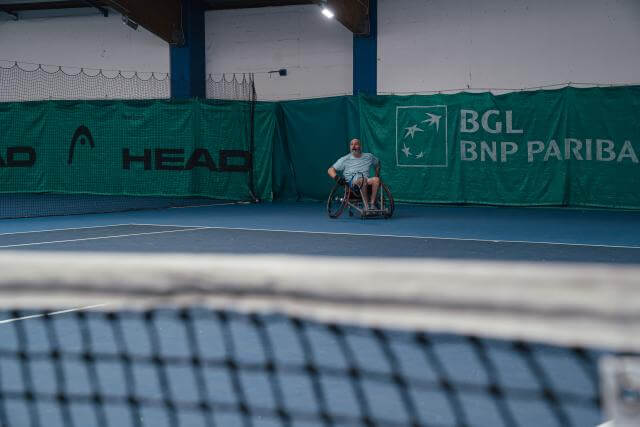 A man in a wheelchair, from a distance, as he plays tennis.