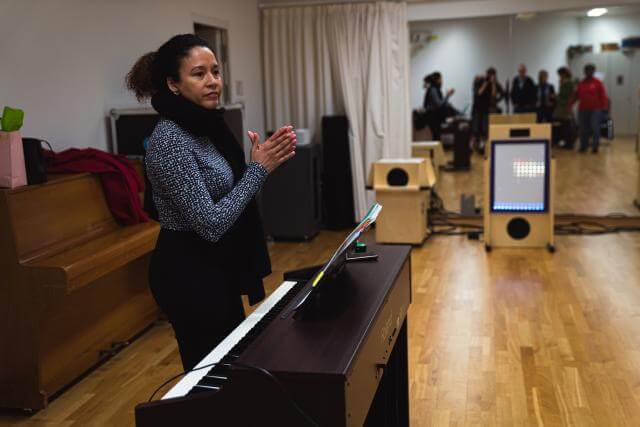 Une femme se tient debout derrière un piano, les mains jointes comme pour applaudir.