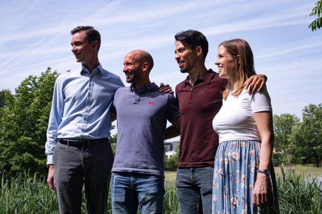 portrait of three men and one woman in front of a little pond
