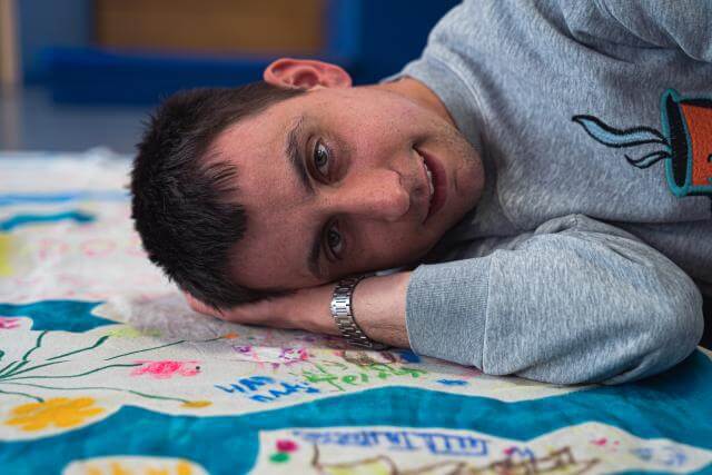 un homme est couché par terre sur un drap et regarde la caméra