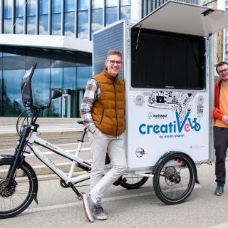 Deux jeunes hommes de l'assciation Youth4Climate, portraités devant un bâtiment au Kirchberg avec leur vélo du projet Creativelo.