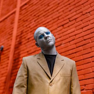 portrait de l'artiste Max Thommes devant un mur en briques rouges