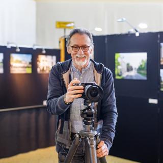 Portrait de Philippe Malaise, devant son exposition photos avec un appareil photo à la main
