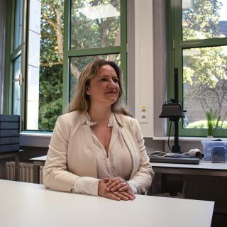 Une femme assise à coté d'une table, son regard tourné vers la droite.