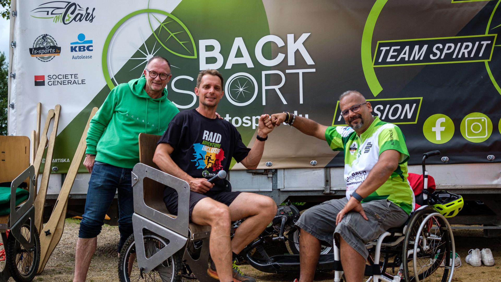 Portrait de trois hommes devant un camion sur lequel est marqué Back to Sport. Deux des hommes sont assis dans des fauteuils roulants.