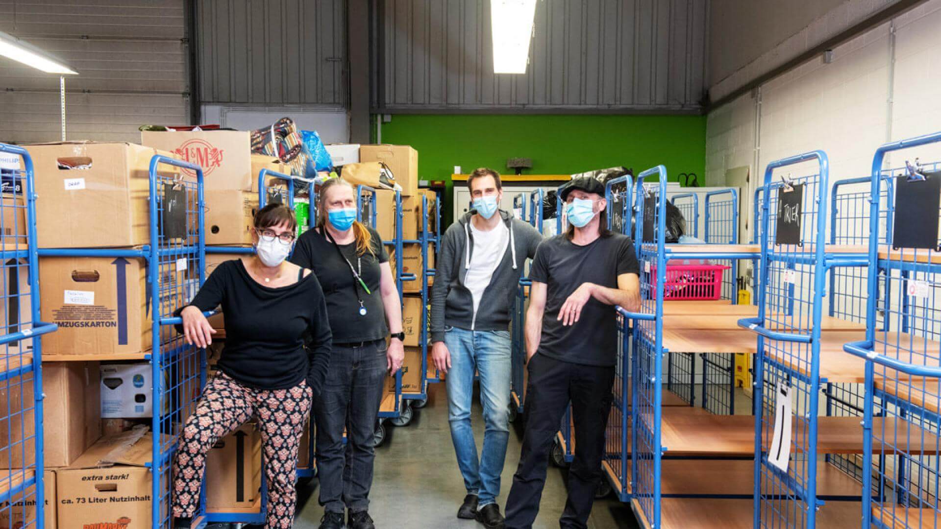 quatre personnes portant des masques respiratoires dans un atelier comportant des chariots à roulettes