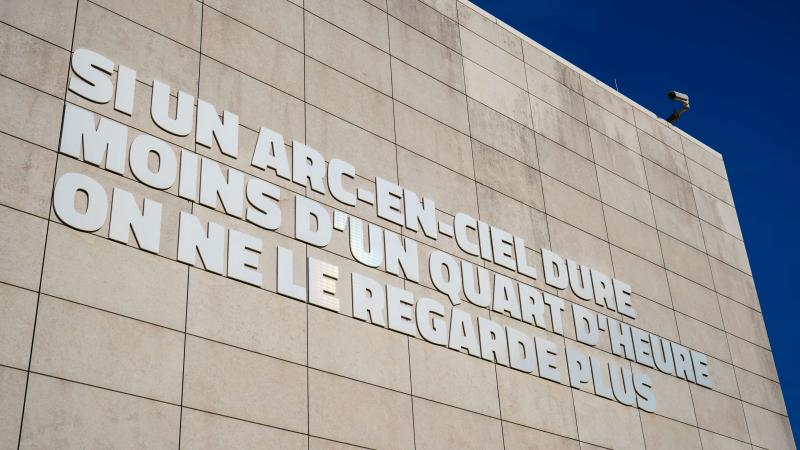 Photo de la façade du bâtiment de l'Œuvre Nationale avec la phrase "Si un arc-en-ciel dure moins d'un quart d'heure on ne le regarde plus"