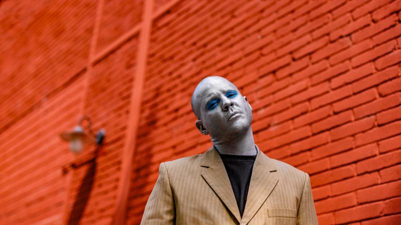 Portrait of the artist Max Thommes in front of a red brick wall.