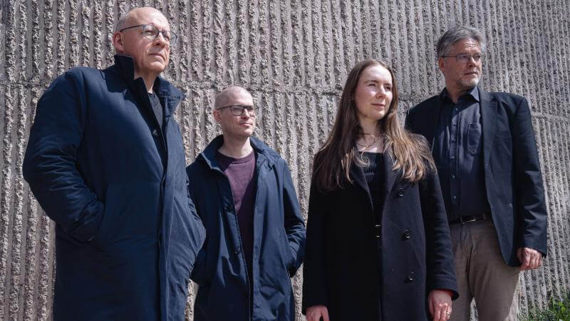 Portrait de quatre hommes et une femme devant un mur en béton