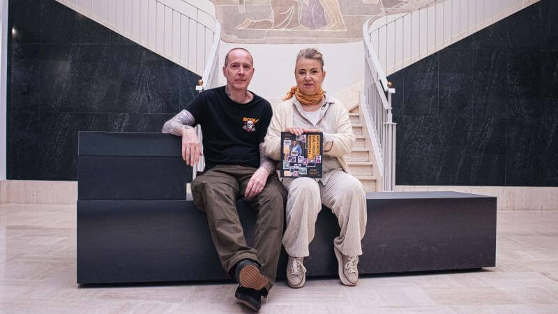 un homme et une femme sont assis sur un banc dans l'entrée du Musée National de la Résistance et des Droits Humains